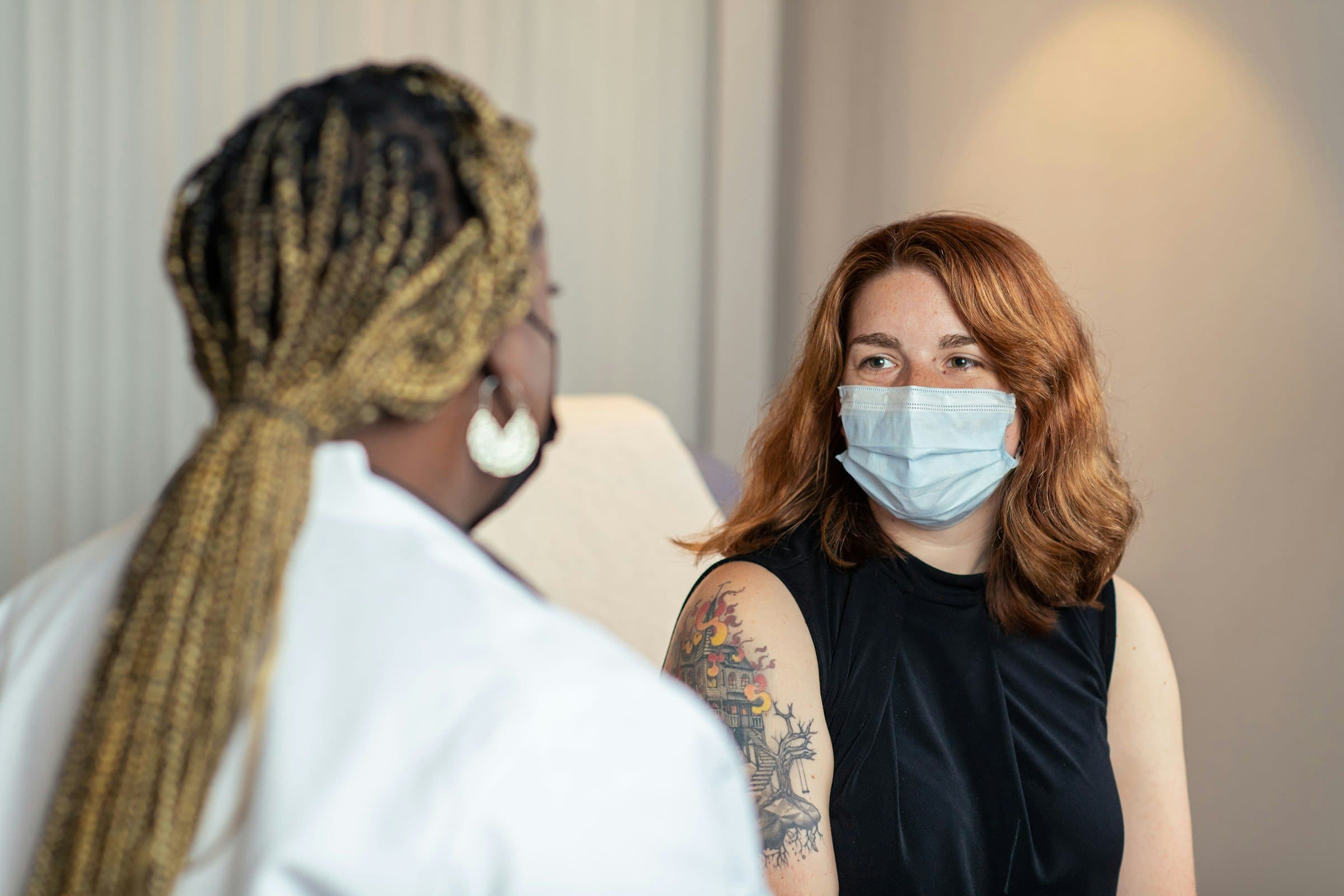 A clinician talks with a patient in a consulting room. Both wear surgical masks.