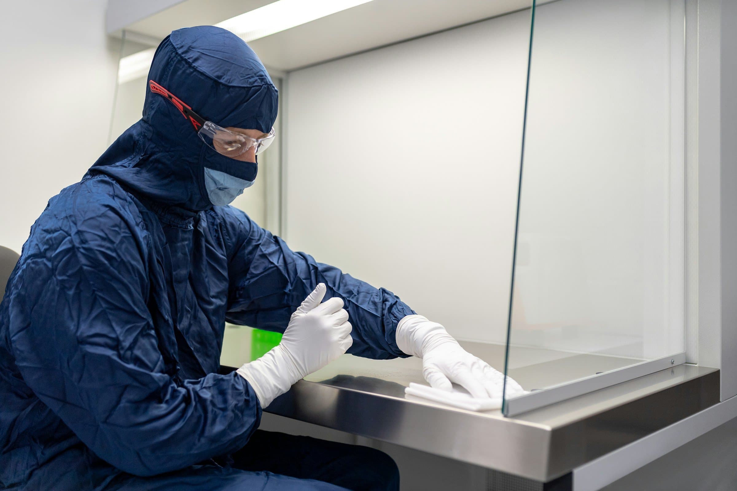 A technician in a cleanroom gown wipes down a laminar-flow hood.