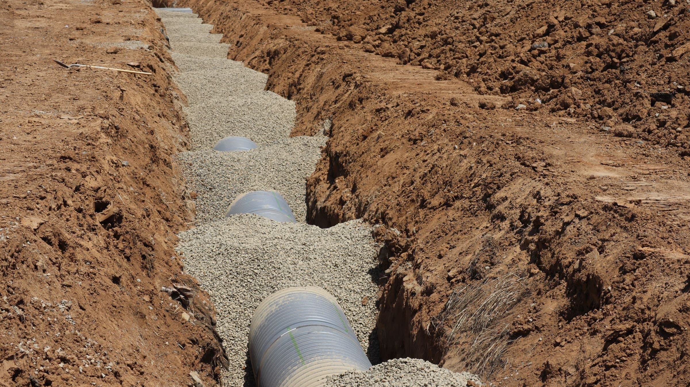 Drainage pipe bedded in gravel in an open trench.